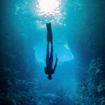 A silhouette of a freediver gliding through a vibrant underwater cave in Tonga.